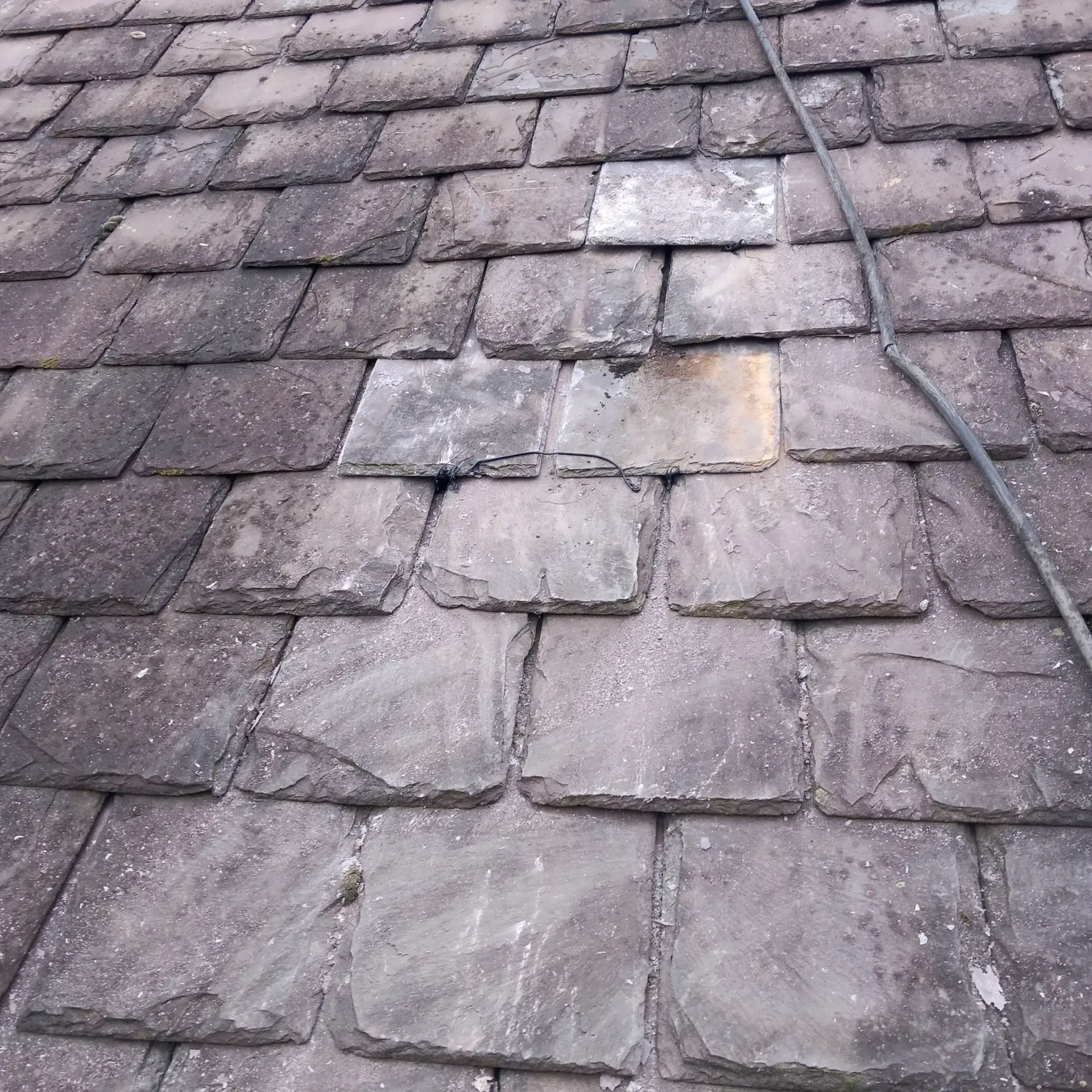 Weathered grey slate roof tiles with visible wear and minor damage, suggesting a need for roof repair or maintenance.