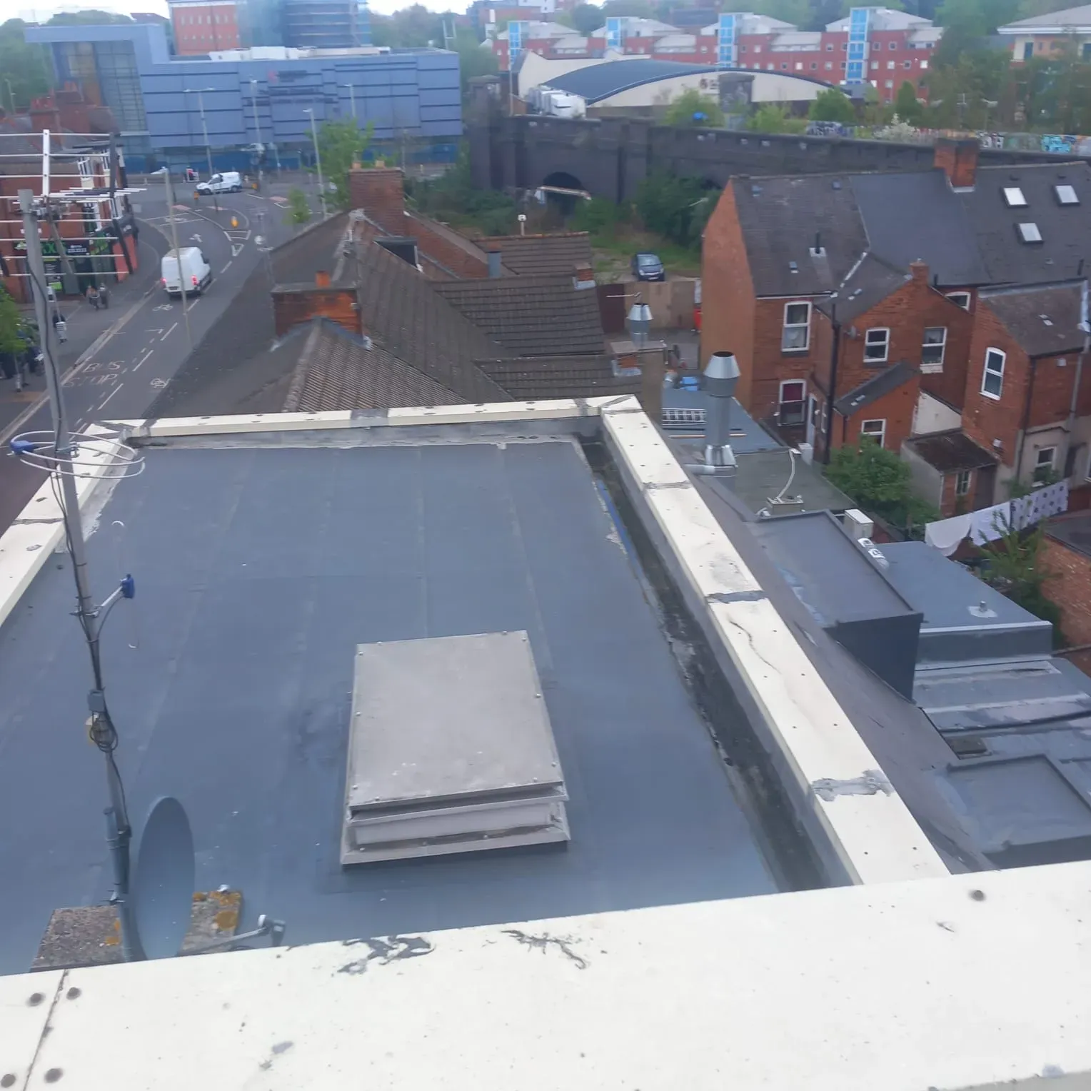 Aerial view of a flat roof in Leicester with antennas, overlooking residential homes, commercial buildings, and a road, highlighting 5 Star Roofing Leicester's diverse service environment.